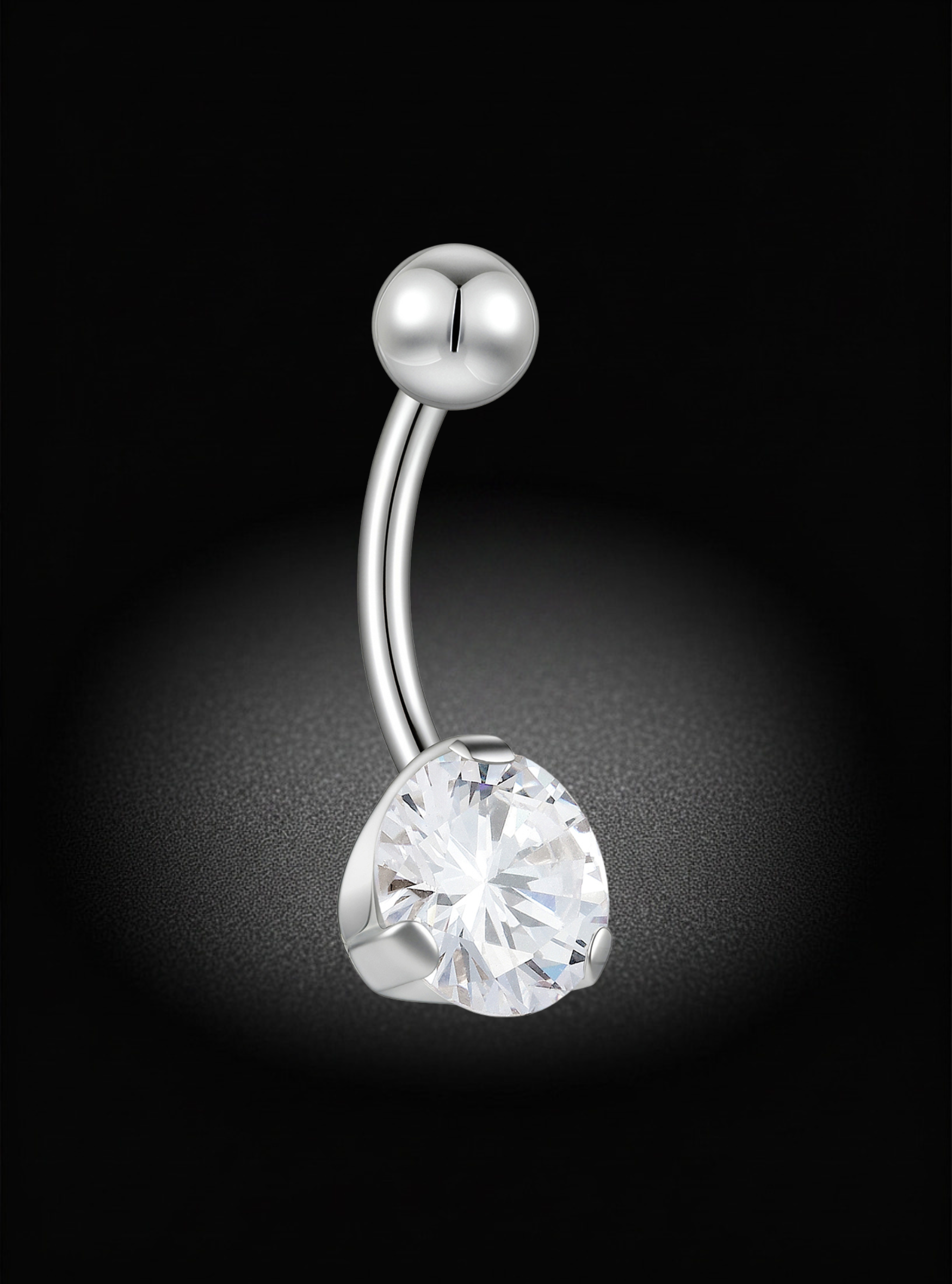 A curved silver-tone belly button ring with a faceted clear heart-shaped gemstone and a small round bead at the top, shown on a black background with a soft glow.