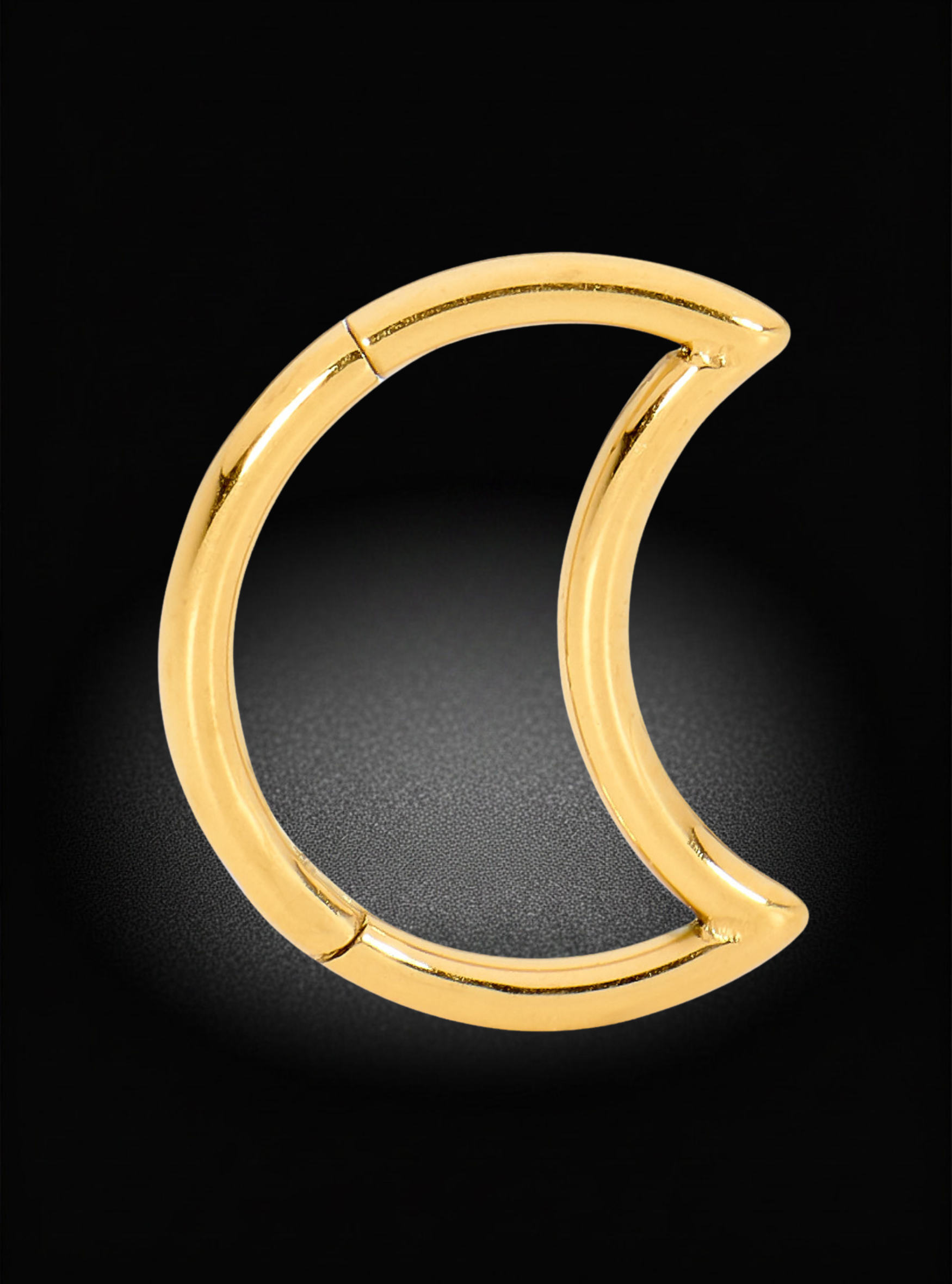 A polished gold crescent moon-shaped ring or hoop earring, shown on a dark black background with a soft spotlight effect.