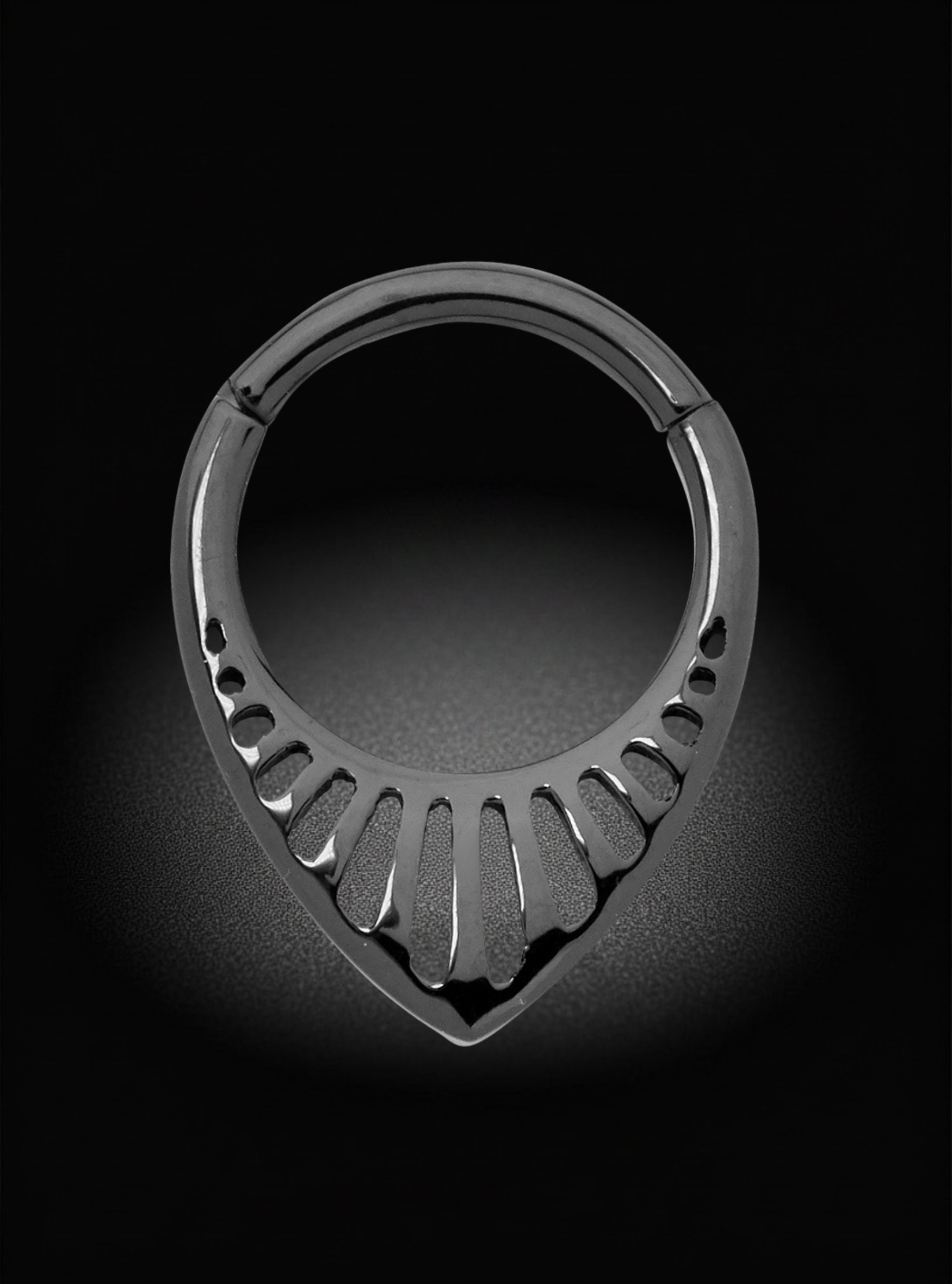 A black titanium hoop piercing ring with a teardrop-shaped lower section and cutout petal-like details, shown on a black background with a spotlight effect.