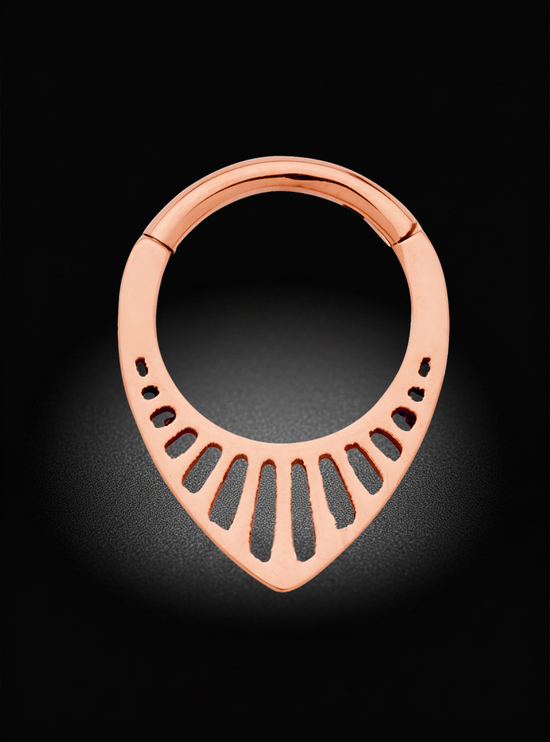 A rose gold body jewelry piece, specifically a teardrop-shaped cartilage piercing ring with a slotted design, shown on a dark background with a spotlight effect.