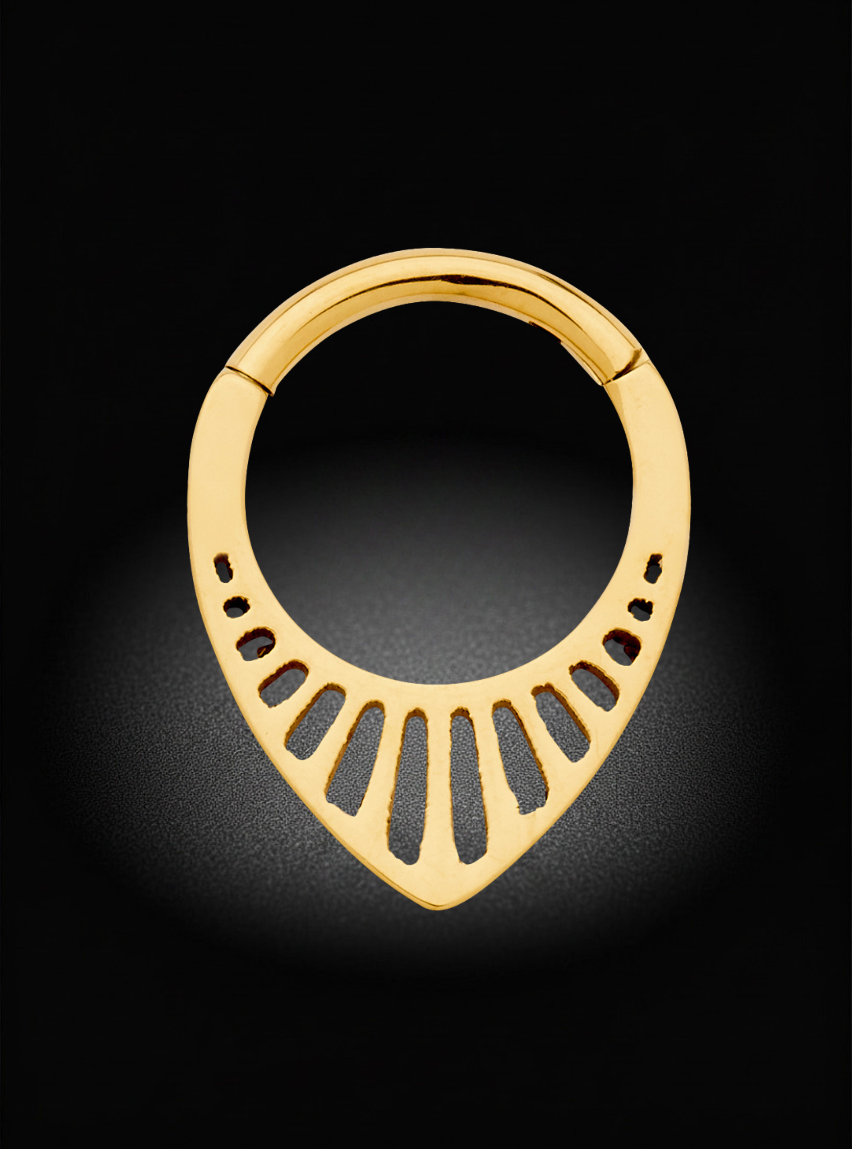 A gold-colored metal hoop earring with a teardrop-shaped lower section featuring cut-out slits, displayed against a dark black background with a soft spotlight effect.