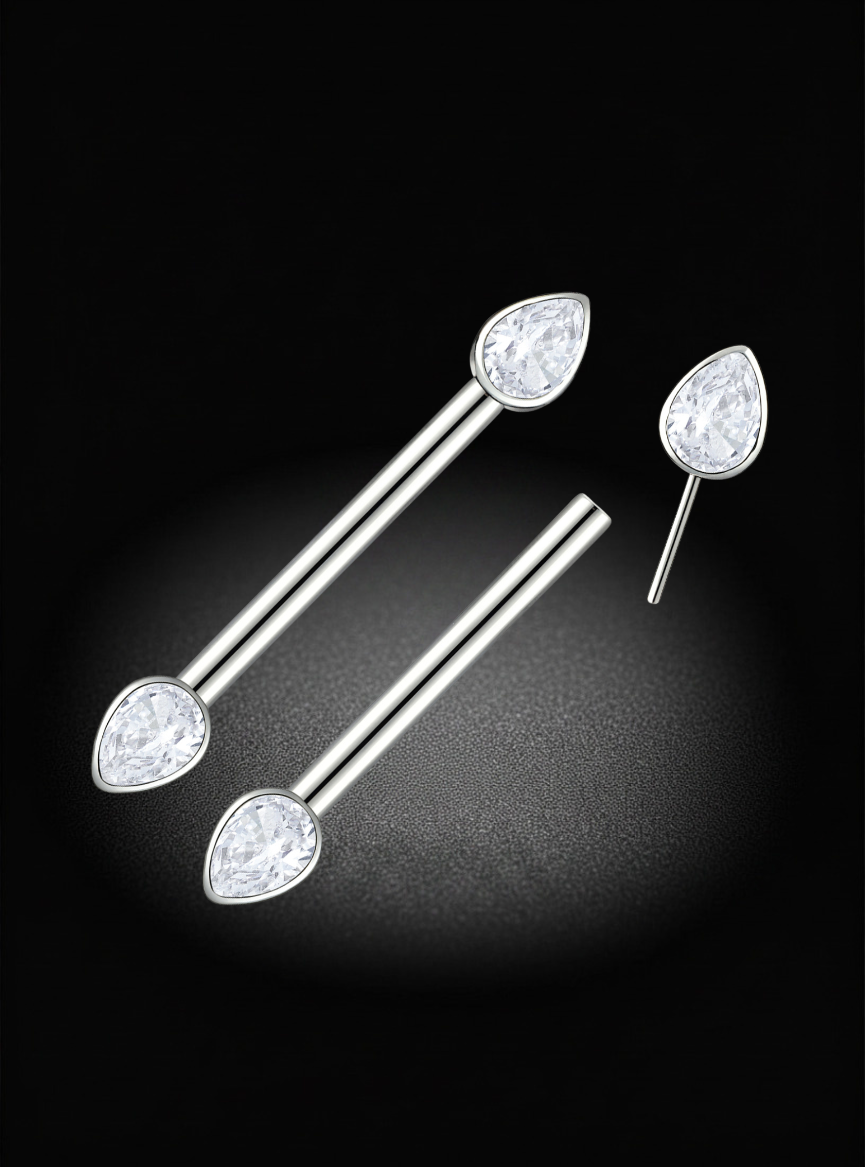 A pair of silver titanium nipple threadless barbell with teardrop-shaped clear gemstones, displayed on a black background with a soft spotlight effect.