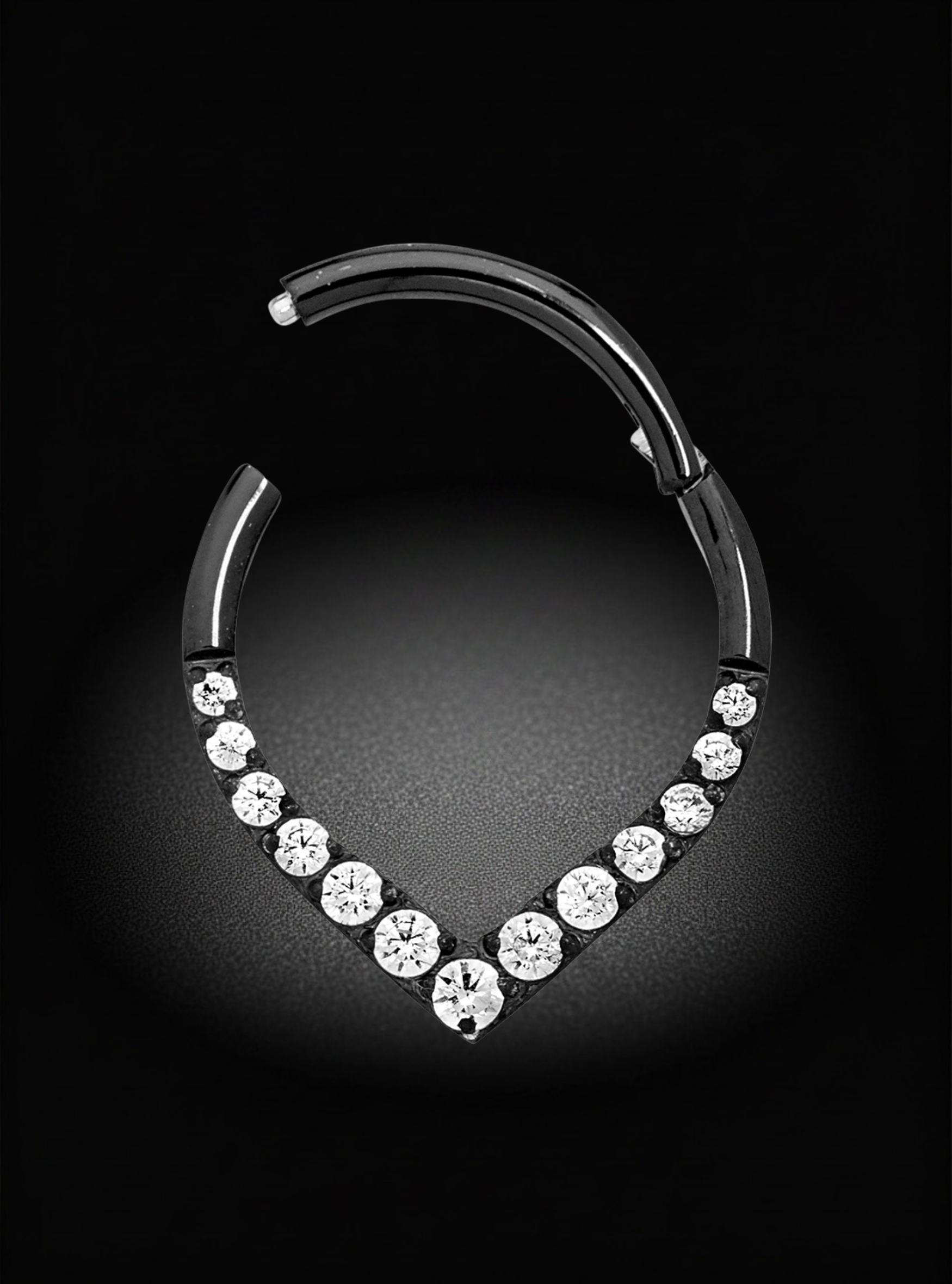 A silver-toned hoop earring with a V-shaped row of clear round gemstones, photographed against a dark black background with a soft spotlight effect.