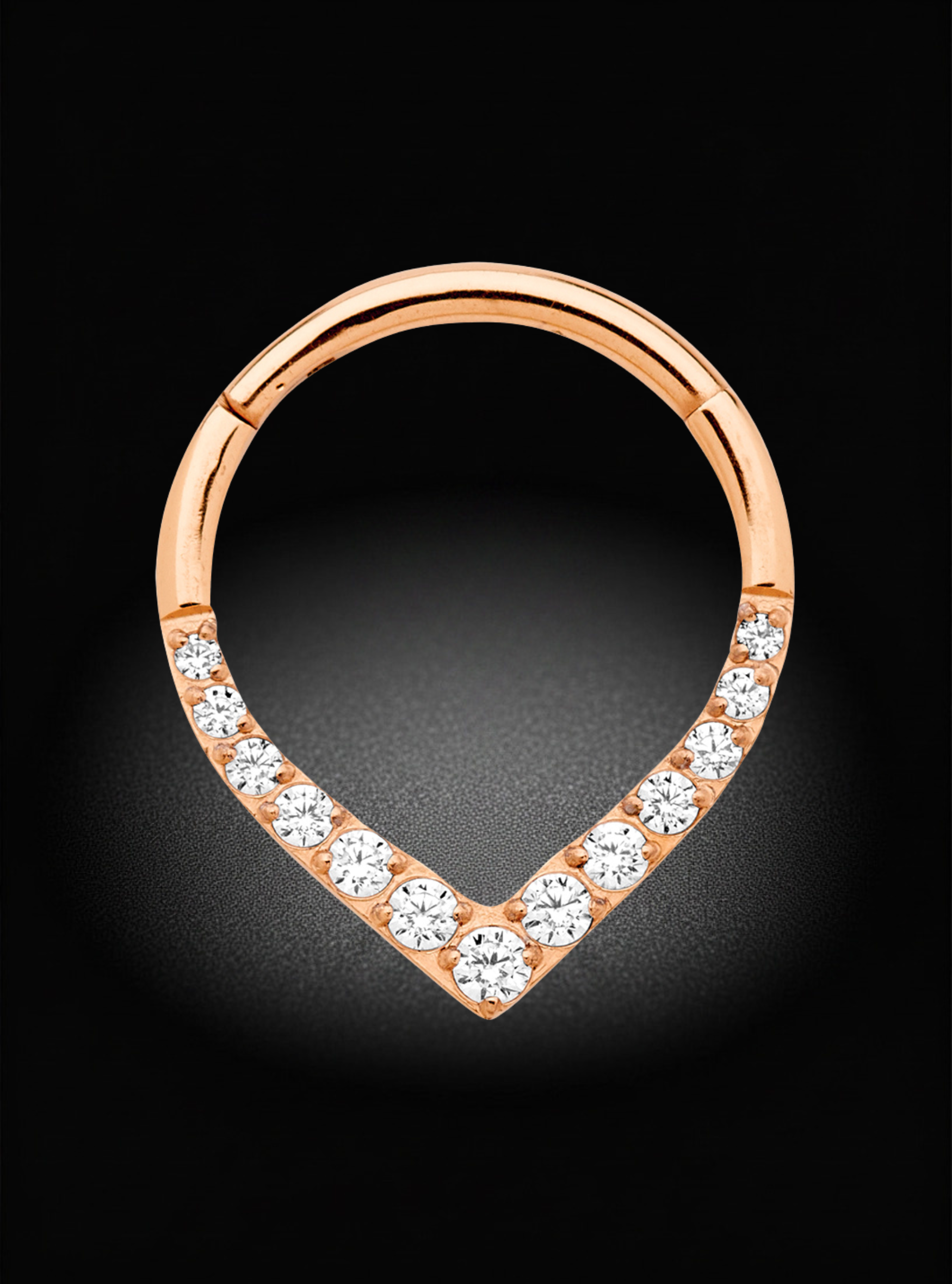 A rose gold huggie hoop ring with a teardrop-shaped bottom section paved with clear round gemstones, set against a dark black background.