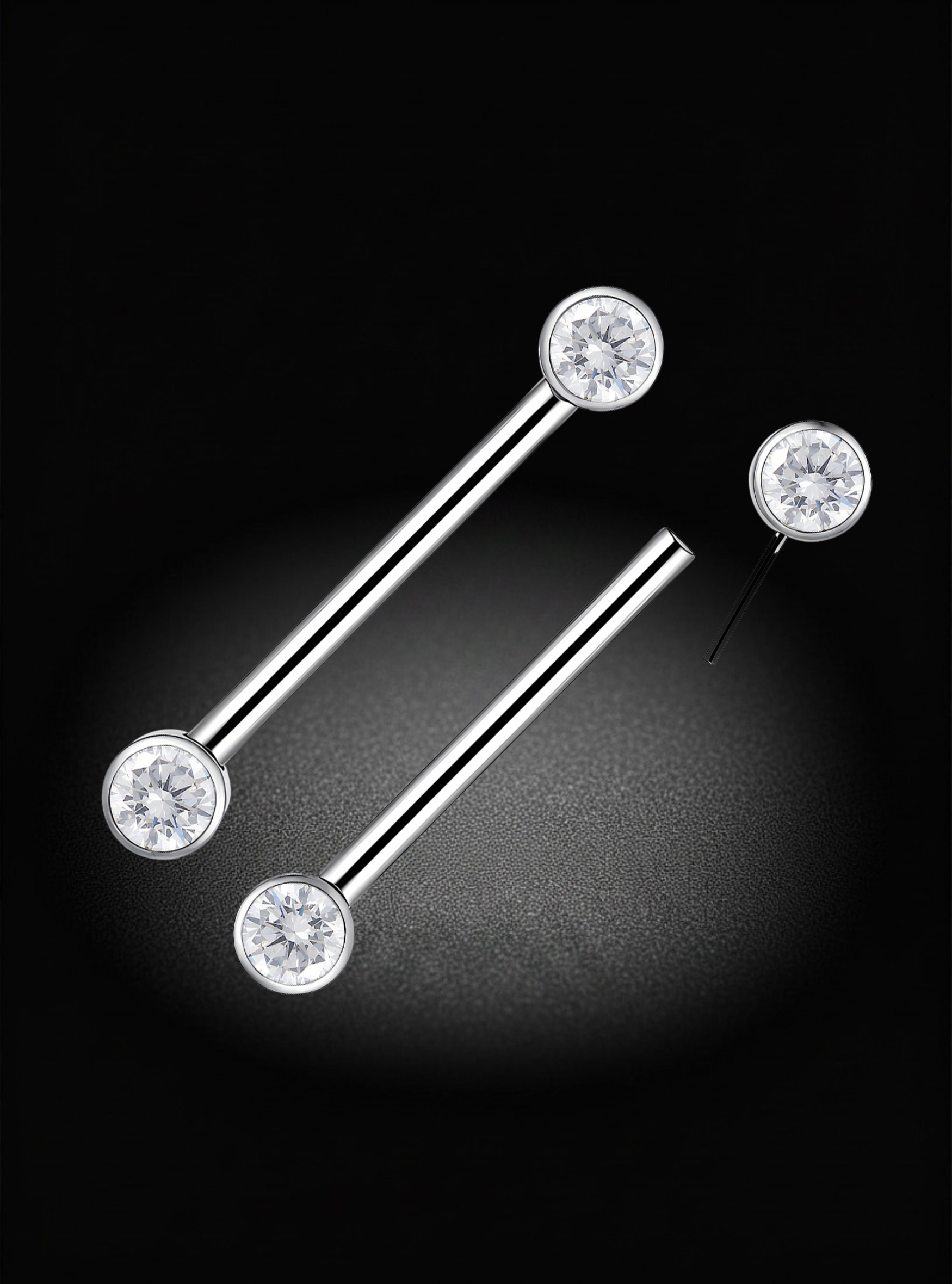 Silver-toned titanium nipple threadless barbell with round clear gemstone, shown on a black background with one earring laid flat and the other angled diagonally.