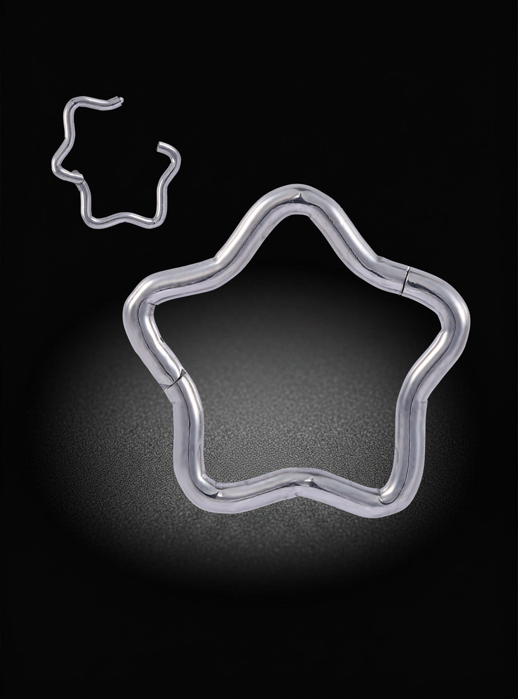 A silver metal star-shaped ring with a small matching star-shaped accessory floating above it, set against a dark black background with a spotlight effect.
