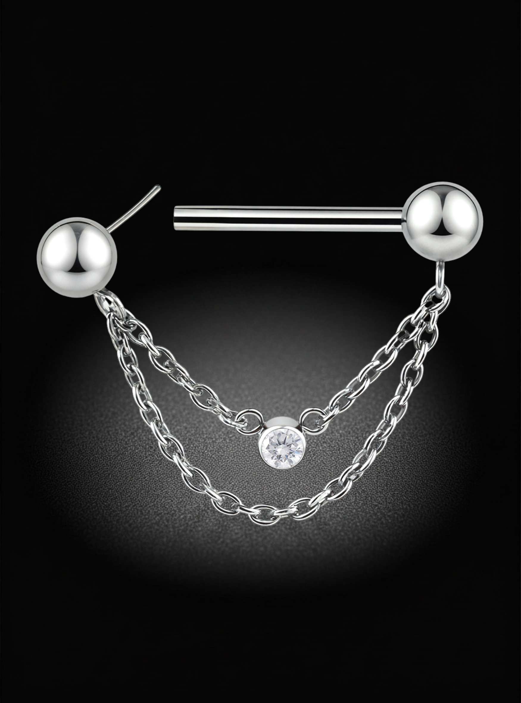 A silver-toned titanium nipple barbell piercing stud with two ball end caps and two draped chain drops, one of which features a small clear round gemstone, shown on a black background.