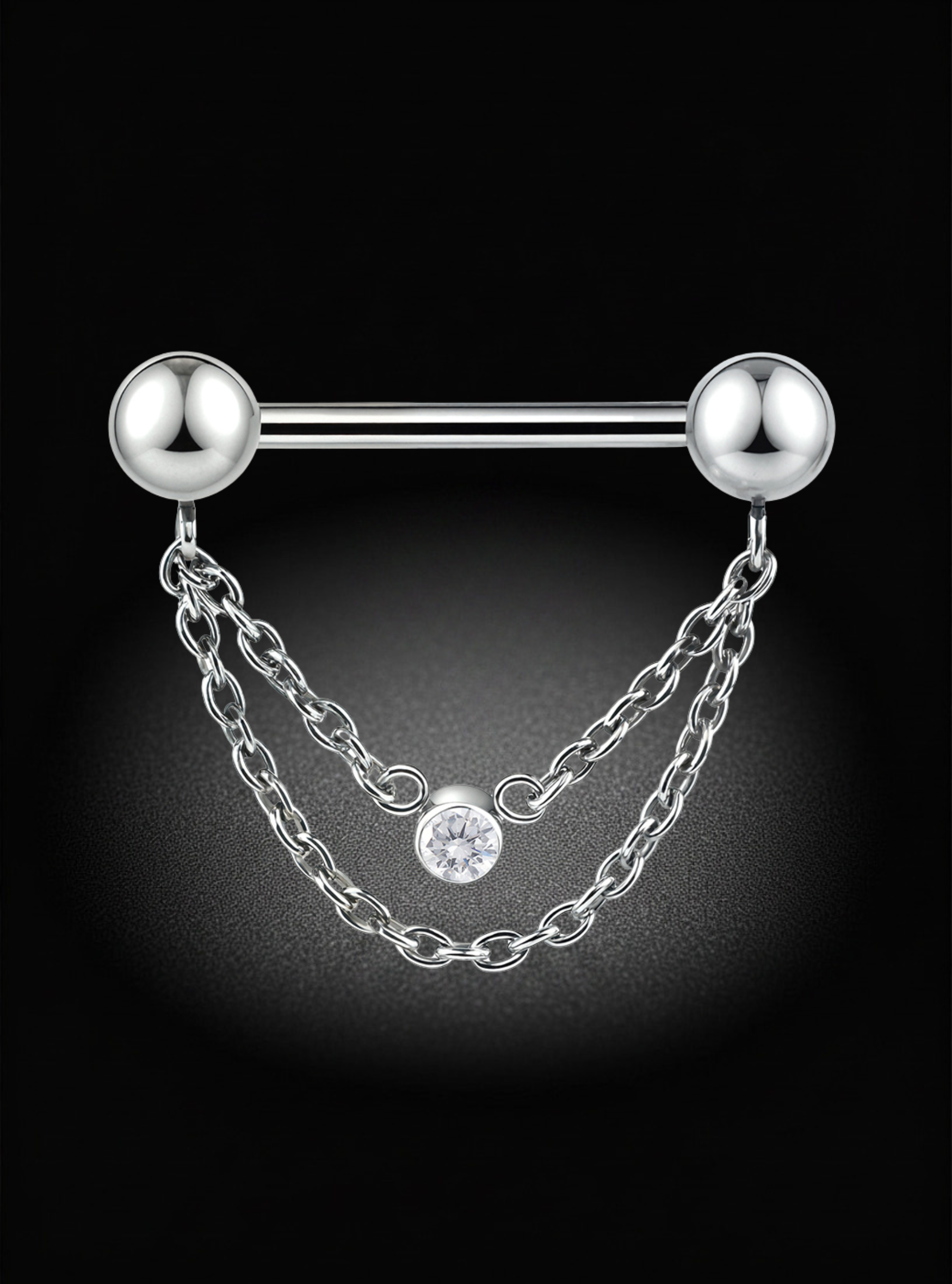 A silver titanium nipple threadless barbell piercing jewelry piece with two spherical ball ends and two hanging chain drops, one of which features a clear round gemstone, set against a dark black background with a soft spotlight effect.