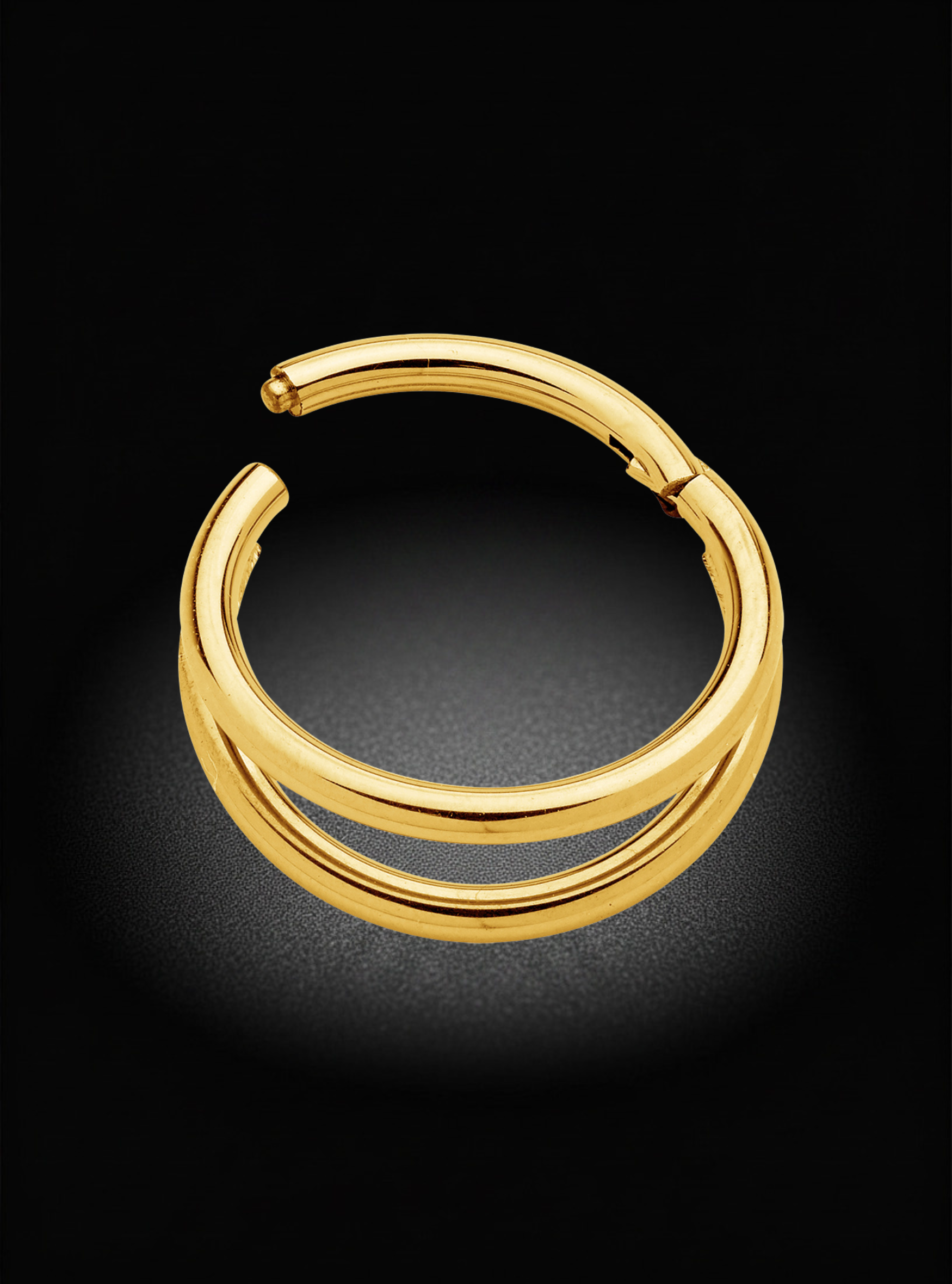 A polished gold huggie hoop earring with a thick, double-stranded wrap design, shown on a dark black background with a soft spotlight effect.