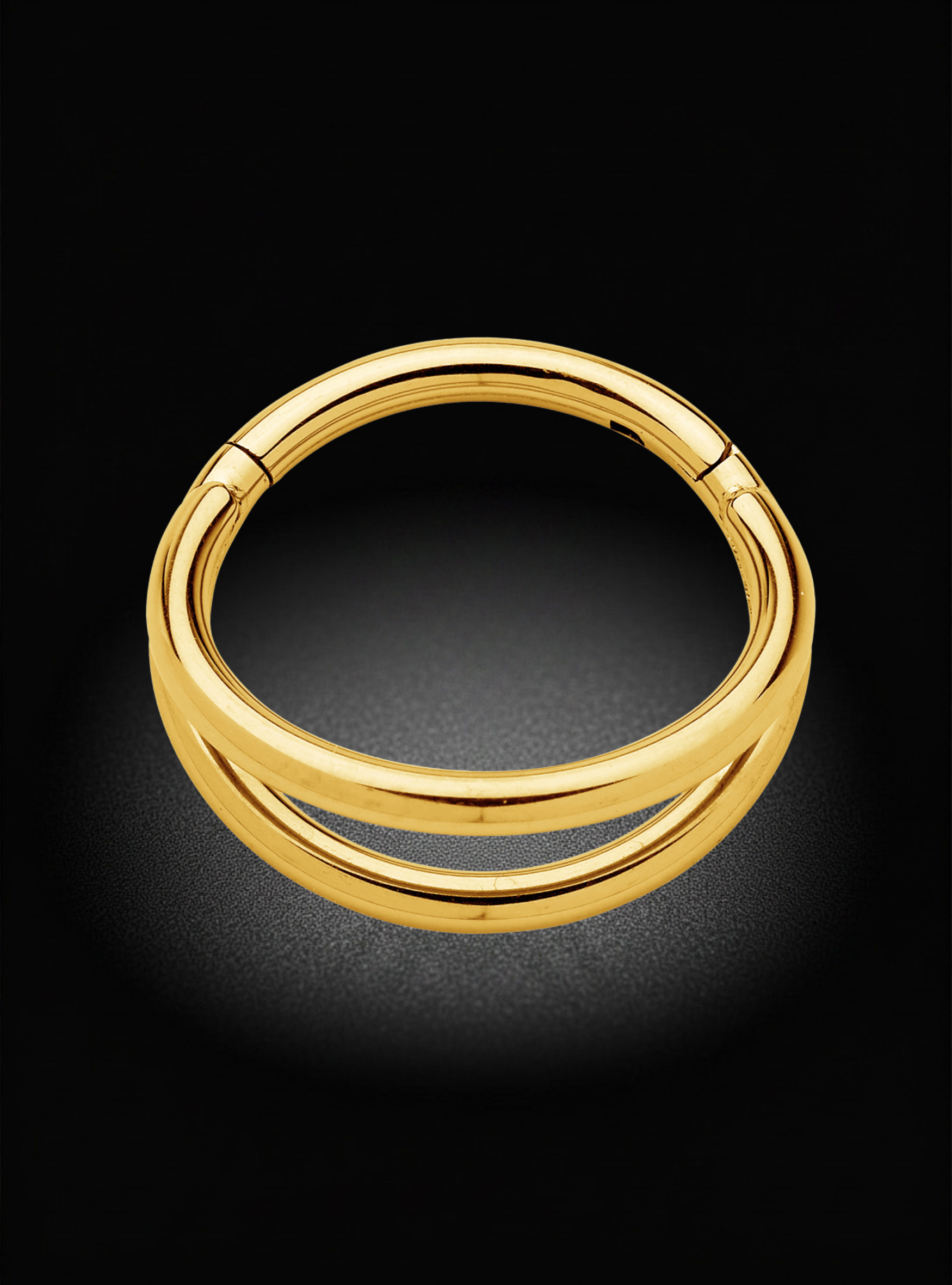 A polished gold-plated double-band hoop ring, shown from a top-down perspective on a dark, reflective surface.