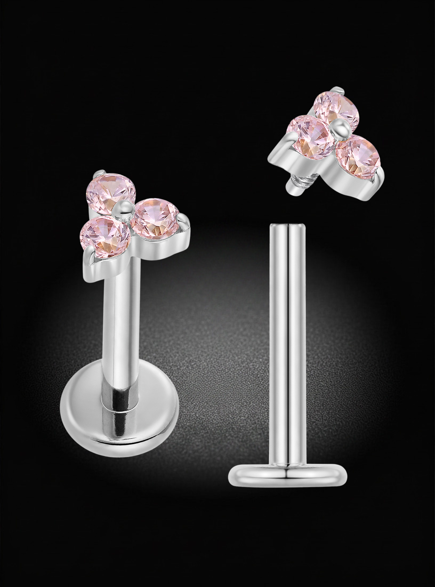 Silver-toned labret earrings with a cluster of three round pink gemstones on the front, shown on a black background with one earring facing forward and the other angled to show the post and backing.